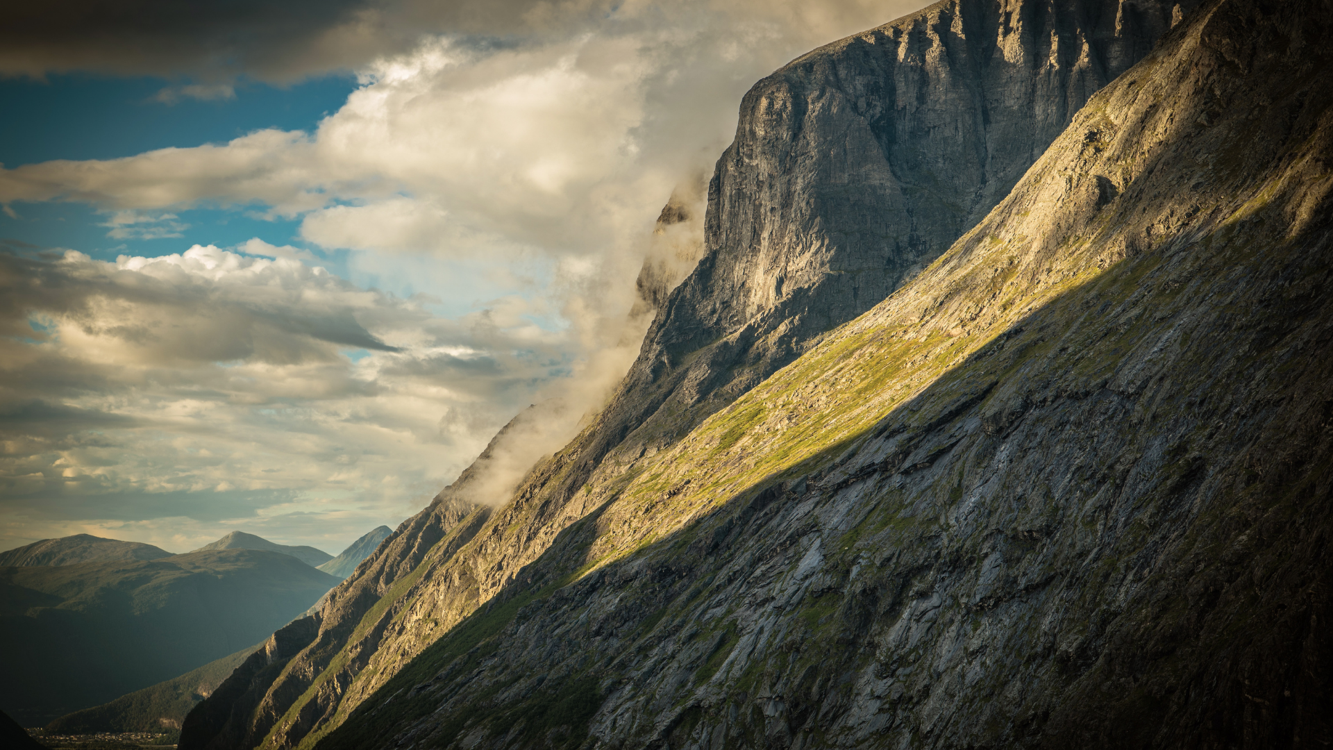 Solen treffer fjellside med himmel og skyer i bakgrunnen